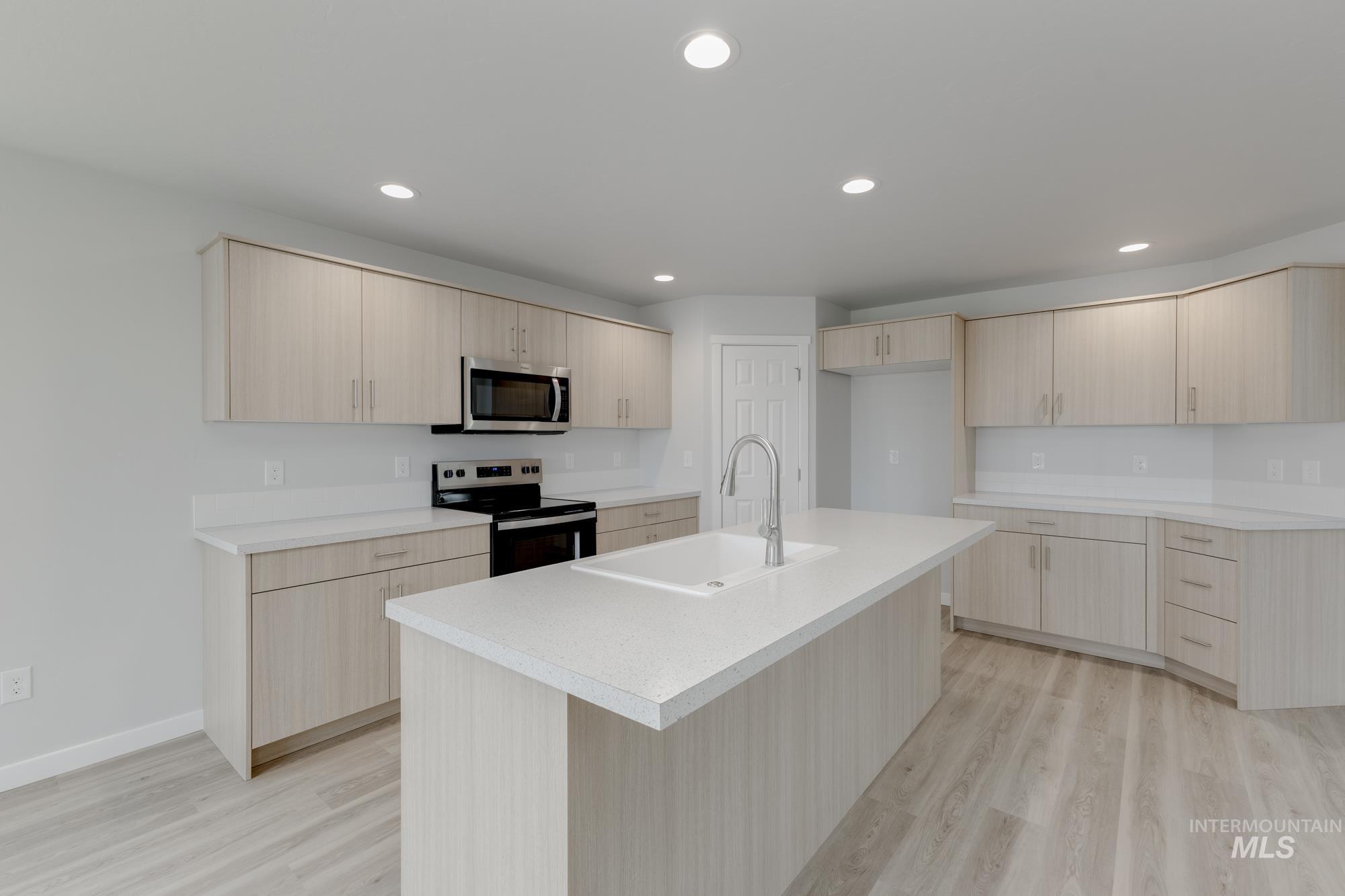 Kitchen with light brown cabinetry, appliances with stainless steel finishes, light countertops, light wood-type flooring, and modern cabinets