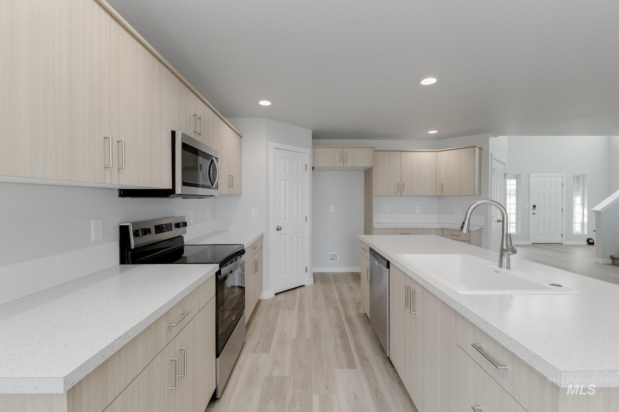 Kitchen with light brown cabinets, stainless steel appliances, modern cabinets, light wood-type flooring, and an island with sink