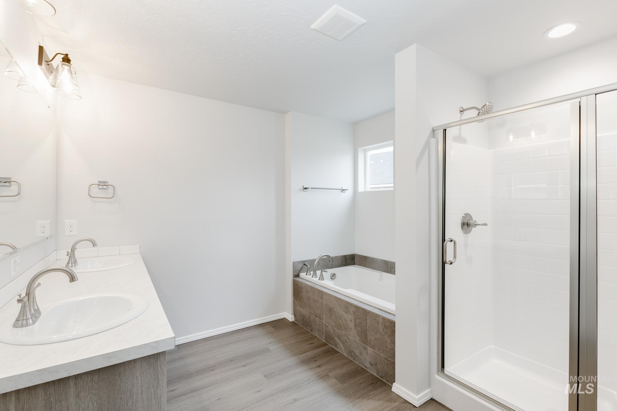 Bathroom with double vanity, light wood-style floors, a shower stall, and a bath