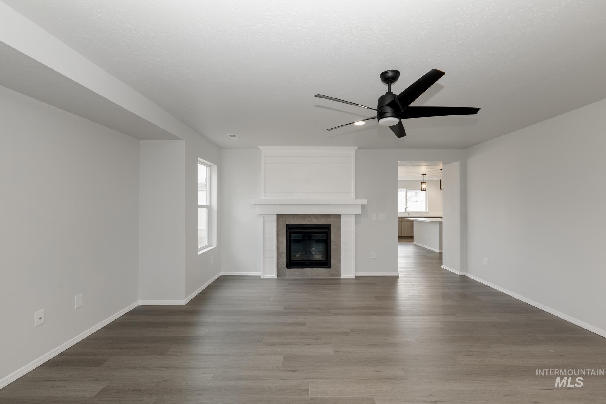 Unfurnished living room with wood finished floors, a tiled fireplace, and ceiling fan