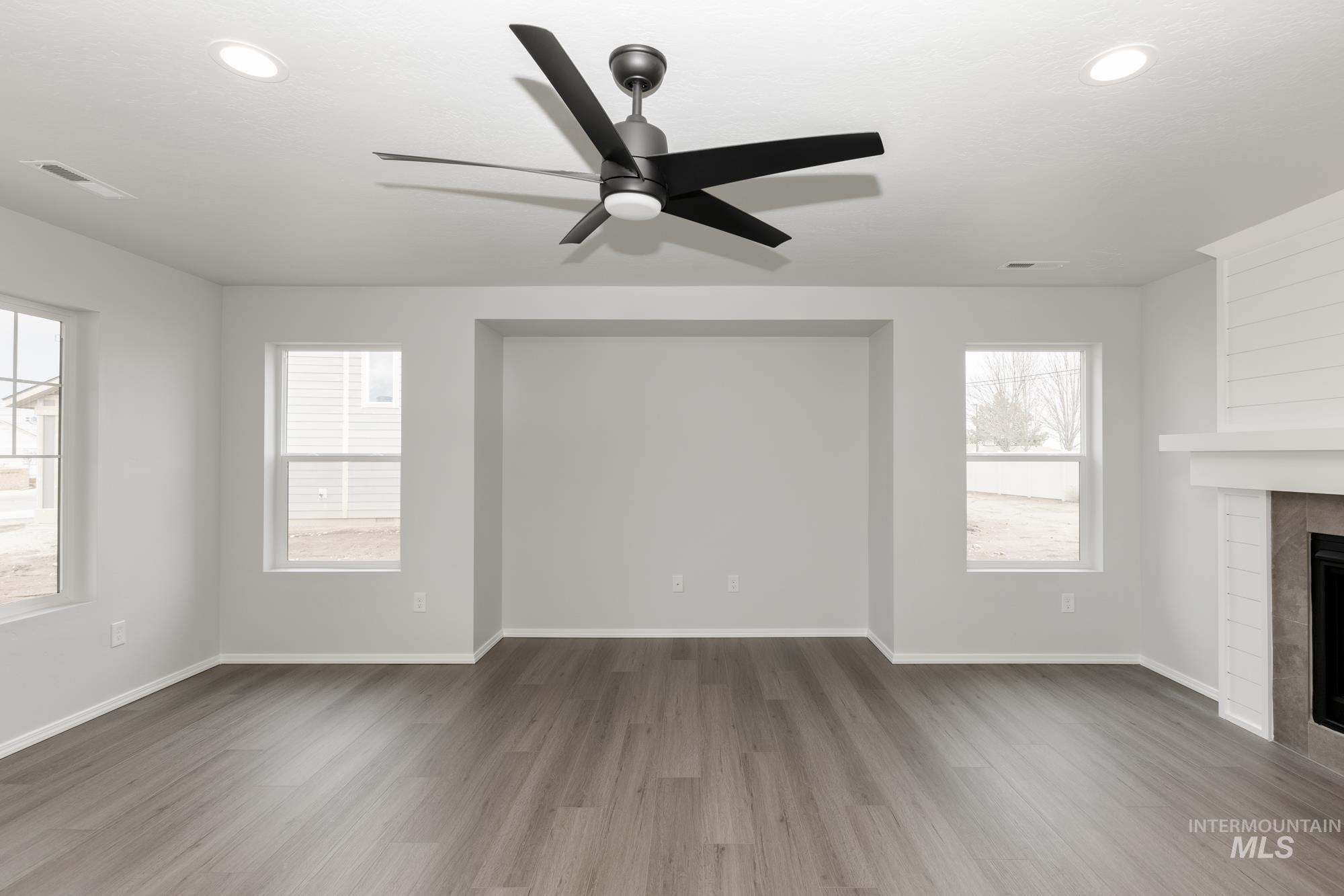 Unfurnished living room featuring wood finished floors, a tiled fireplace, a ceiling fan, and recessed lighting