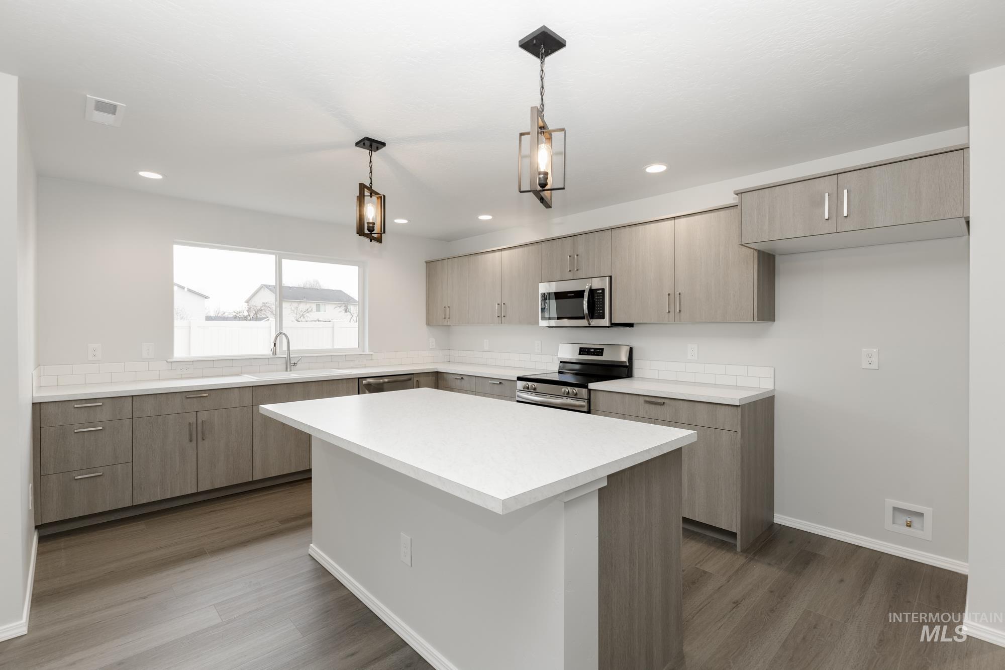 Kitchen with light countertops, a kitchen island, stainless steel appliances, decorative light fixtures, and modern cabinets