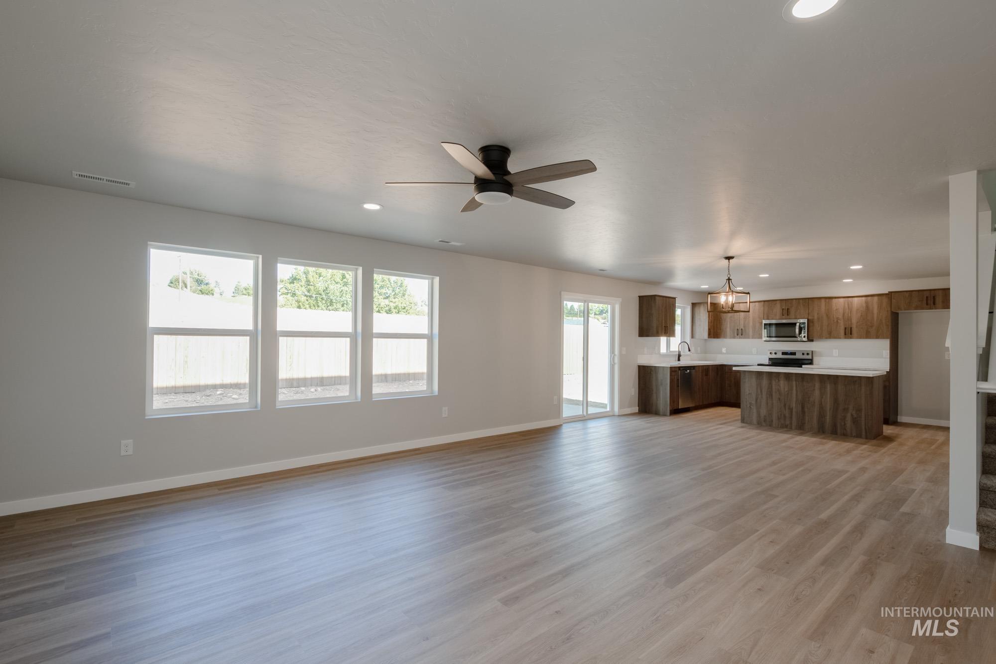 Unfurnished living room featuring recessed lighting, light wood-style floors, ceiling fan, and a chandelier