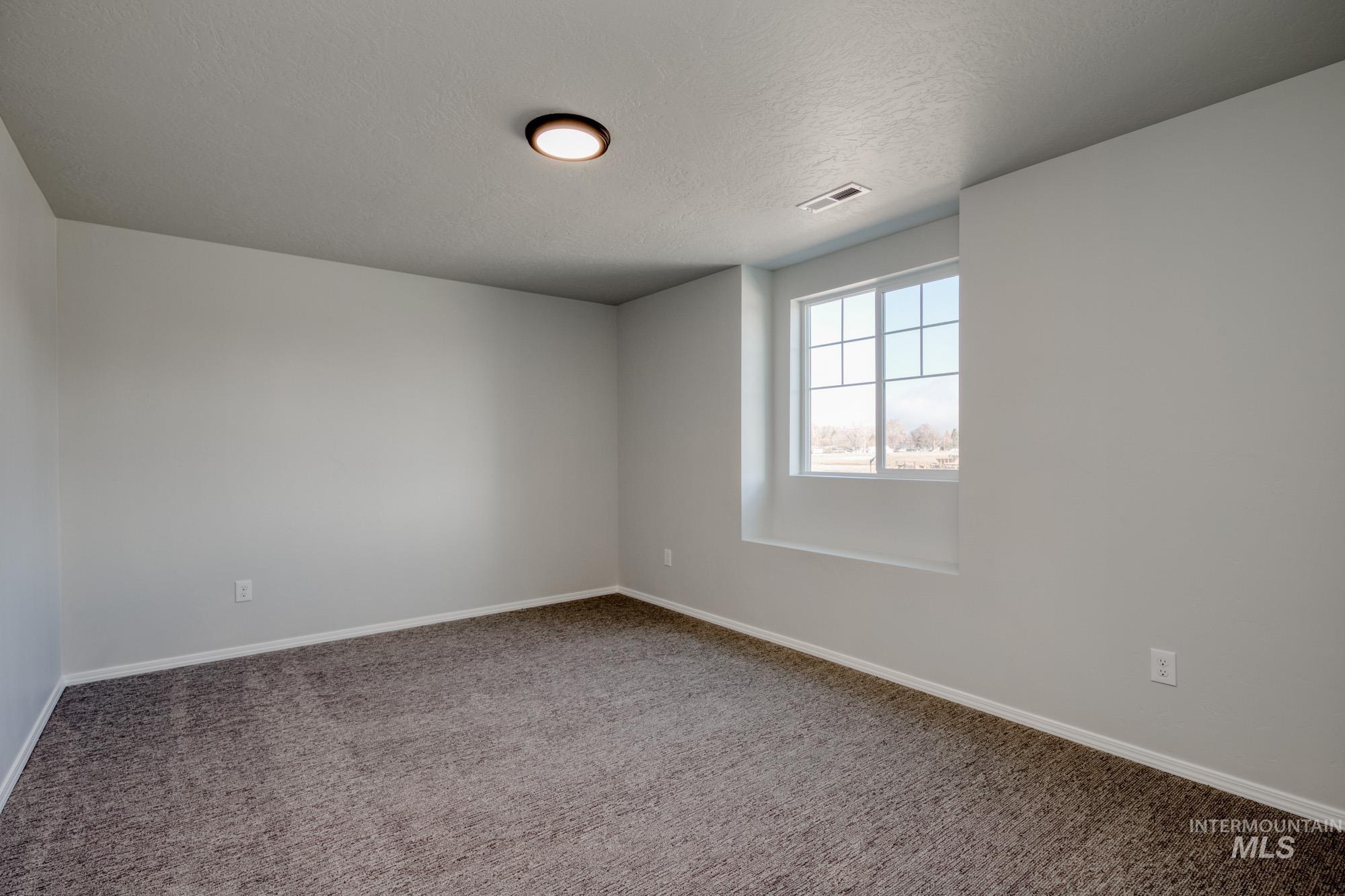 Carpeted spare room with a textured ceiling and baseboards
