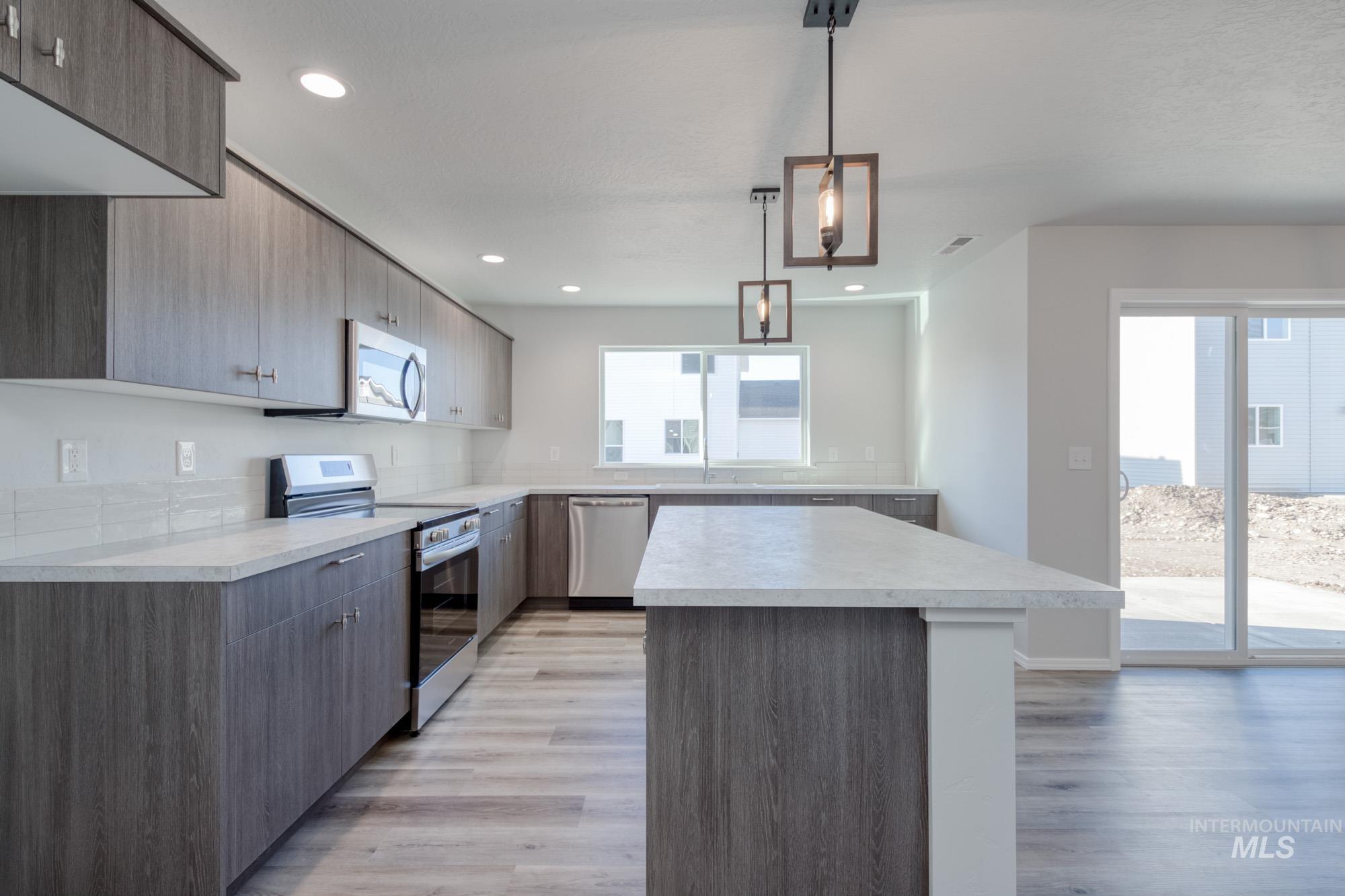Kitchen with light countertops, appliances with stainless steel finishes, decorative light fixtures, a kitchen island, and light wood finished floors