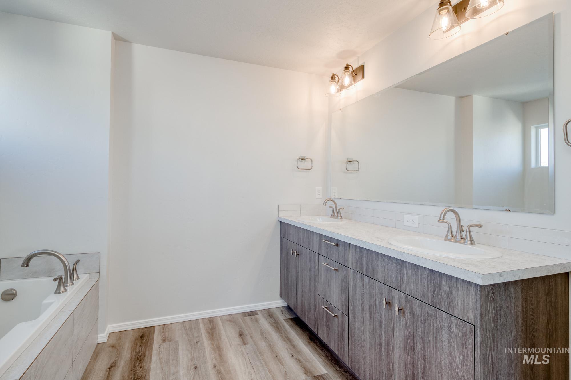Bathroom with double vanity, a garden tub, and light wood-style flooring