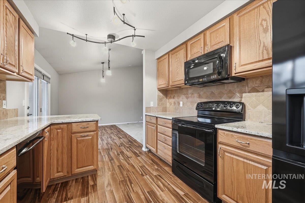 Kitchen with black appliances, light stone counters, lofted ceiling, dark wood-type flooring, and decorative light fixtures