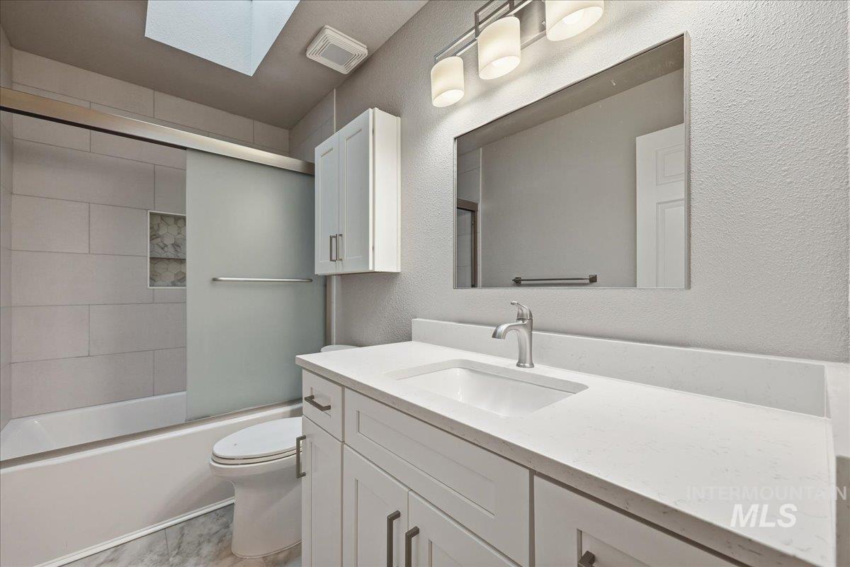 Bathroom featuring a skylight, vanity, a textured wall, and bath / shower combo with glass door