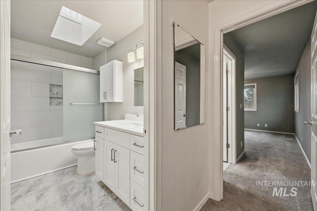 Full bath featuring a skylight, vanity, and bath / shower combo with glass door