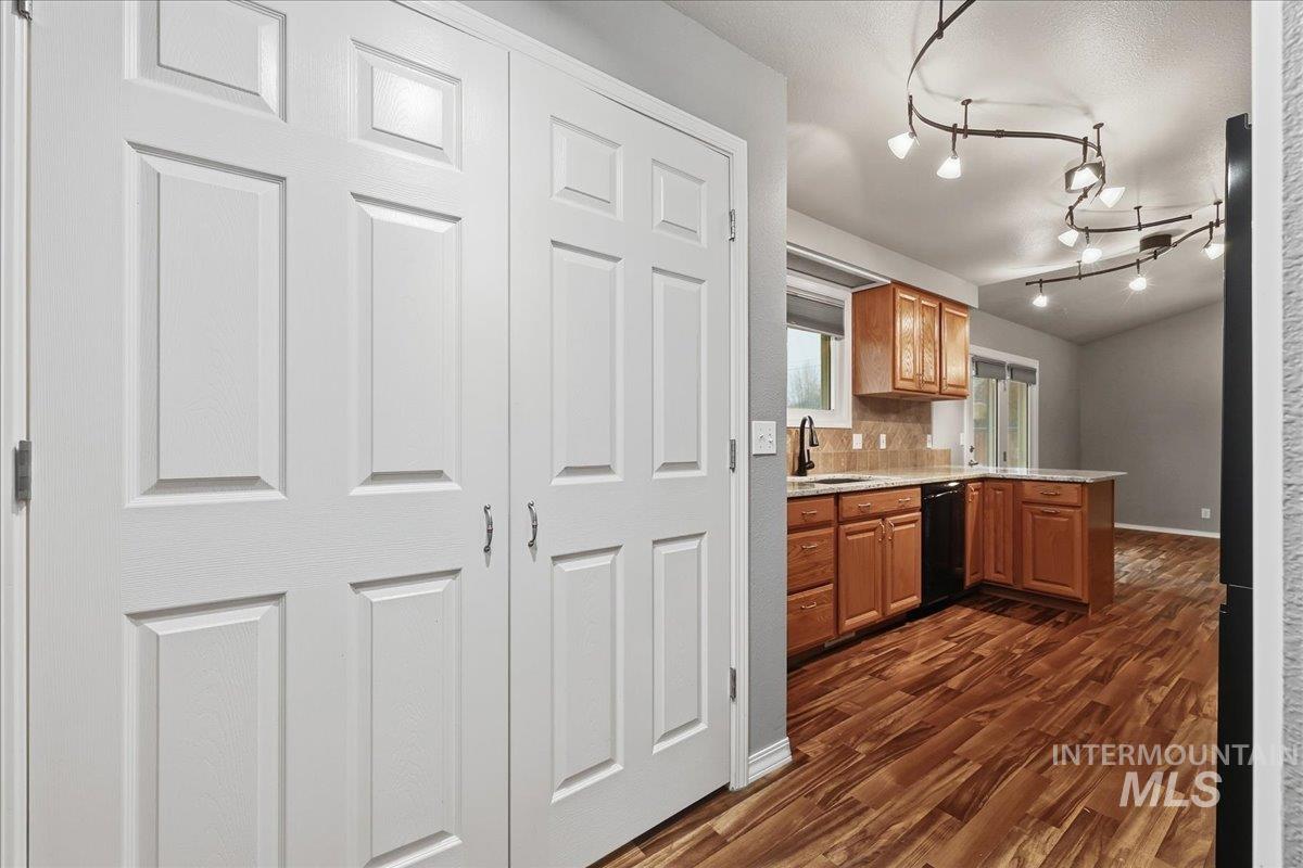 Kitchen featuring a peninsula, brown cabinetry, dark wood-style floors, dishwasher, and decorative backsplash