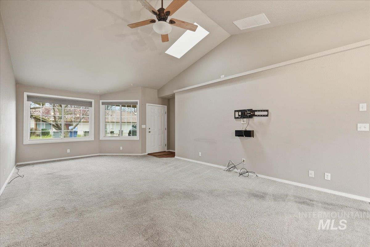 Empty room with a skylight, vaulted ceiling, carpet, and ceiling fan