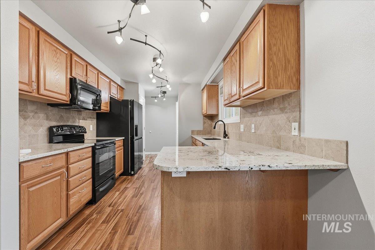 Kitchen featuring light stone countertops, black appliances, tasteful backsplash, and a peninsula