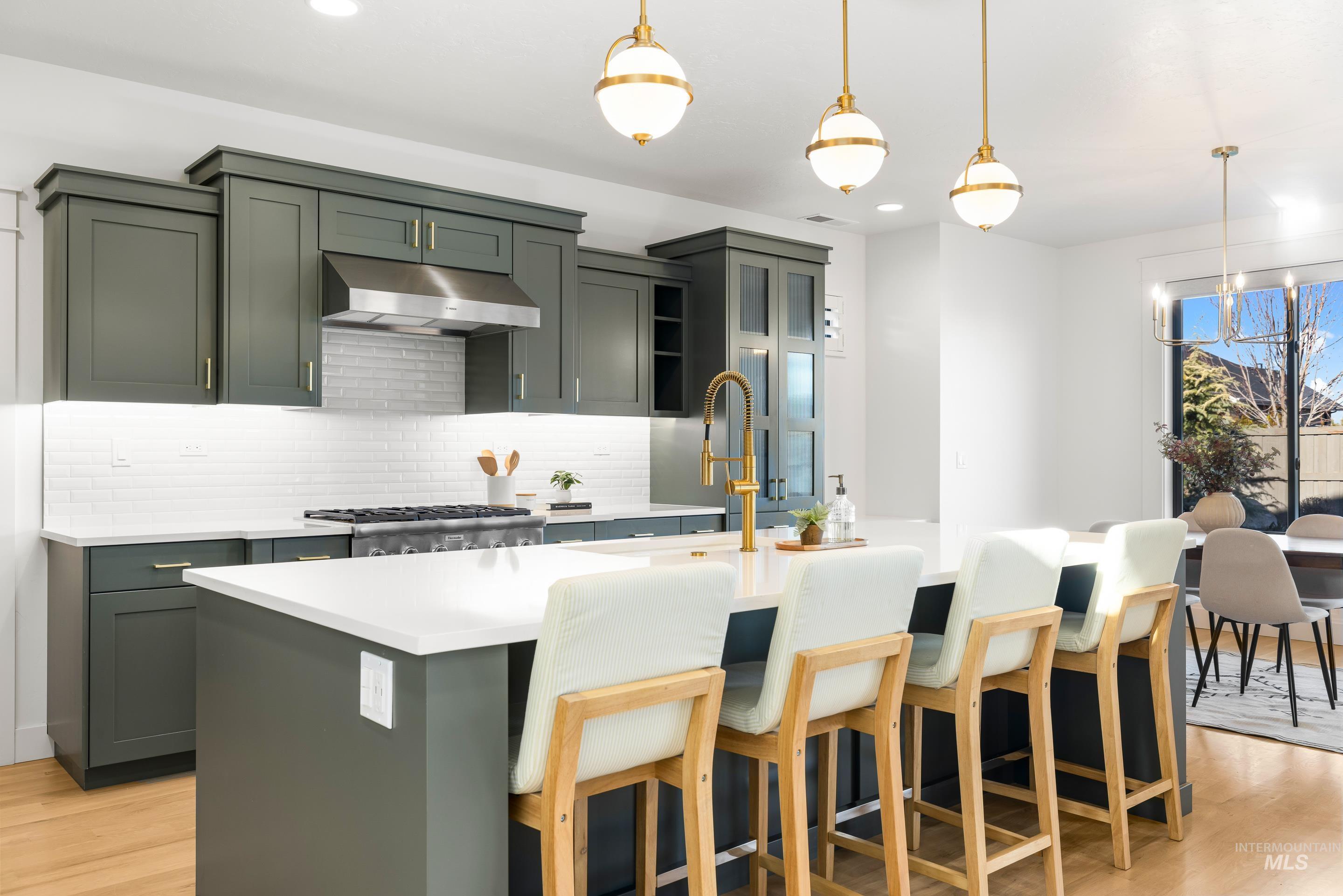 Kitchen with decorative light fixtures, an island with sink, light wood-type flooring, tasteful backsplash, and recessed lighting