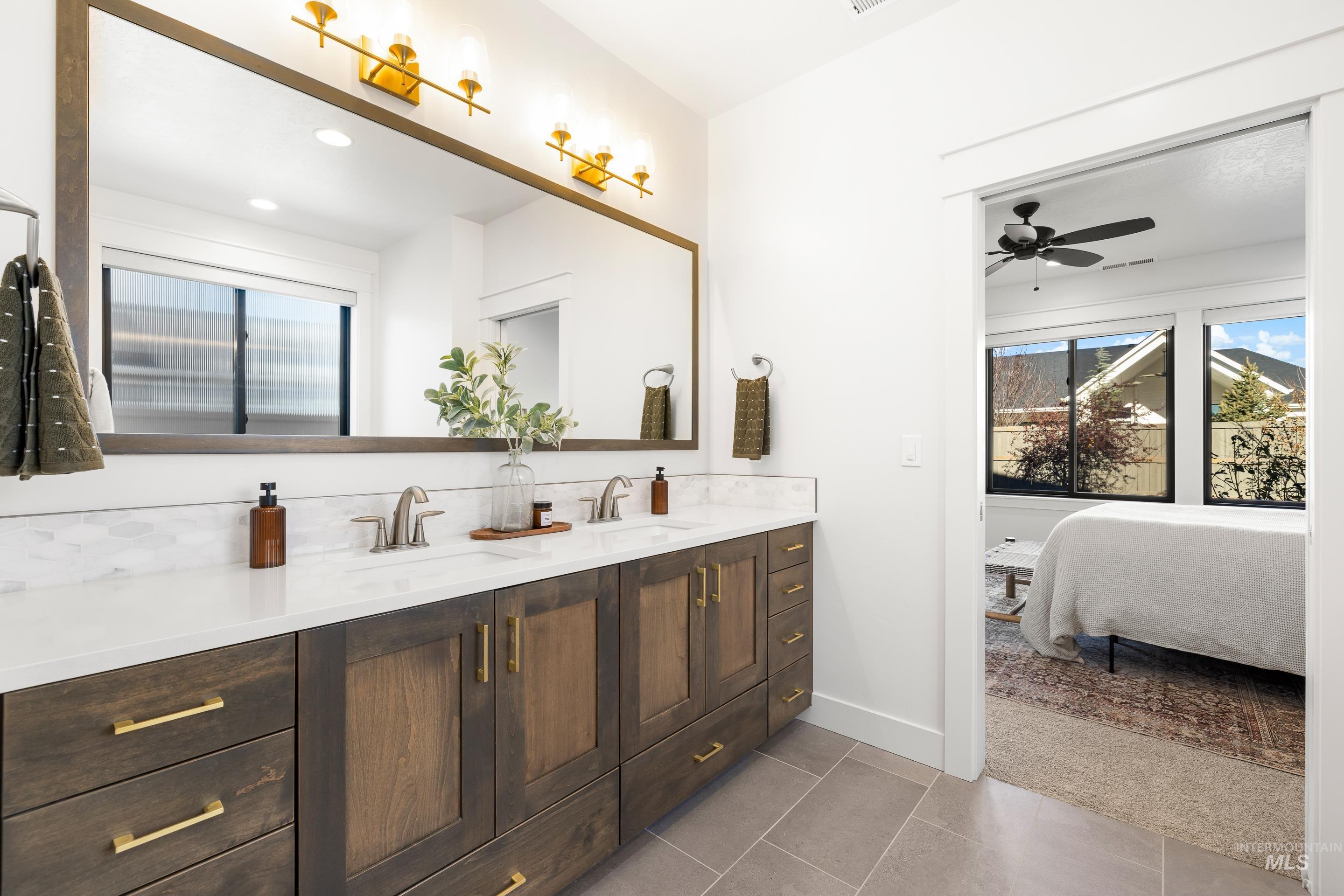 Ensuite bathroom featuring double vanity, dark tile patterned flooring, and ceiling fan