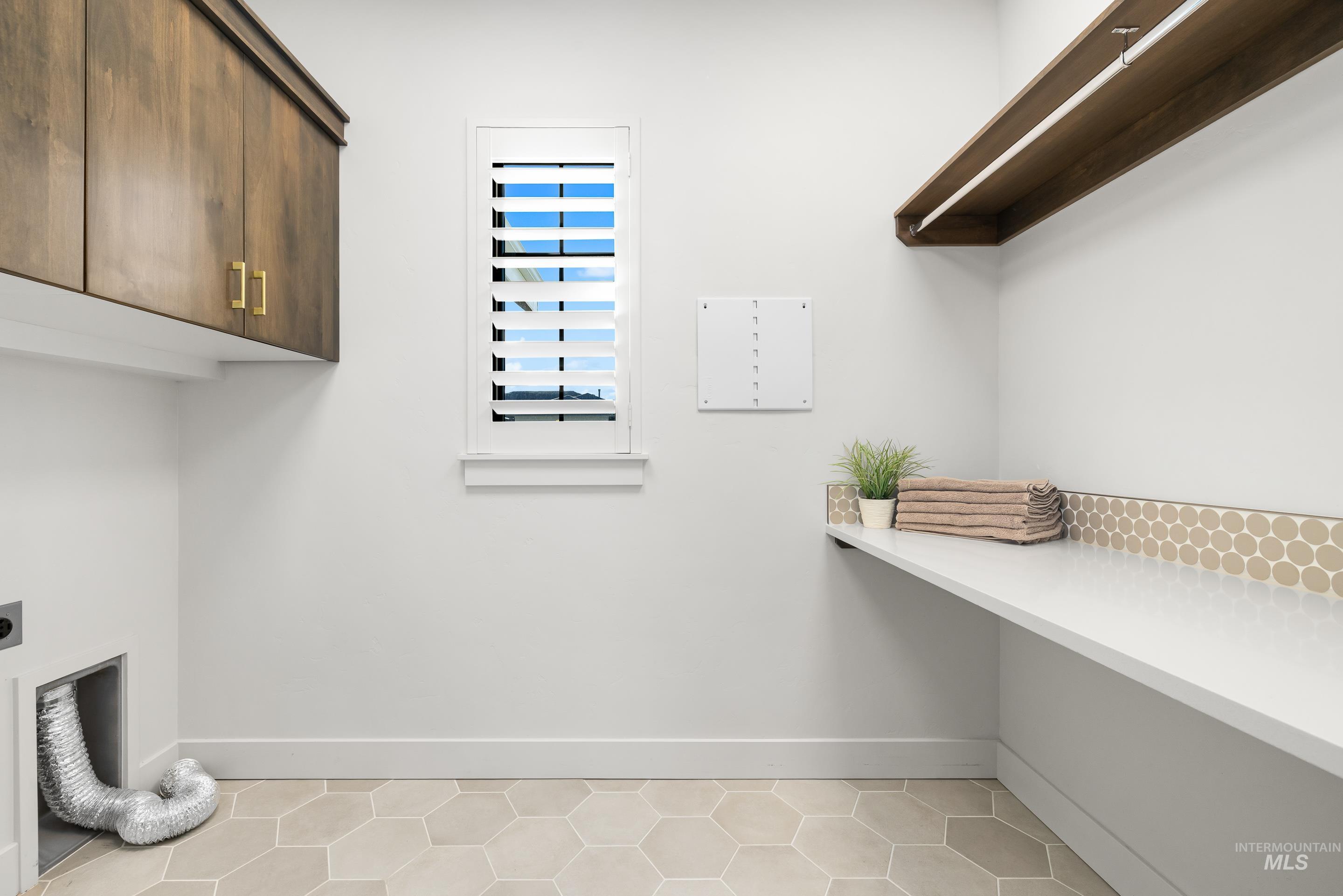 Washroom with electric dryer hookup, light tile patterned floors, and cabinet space
