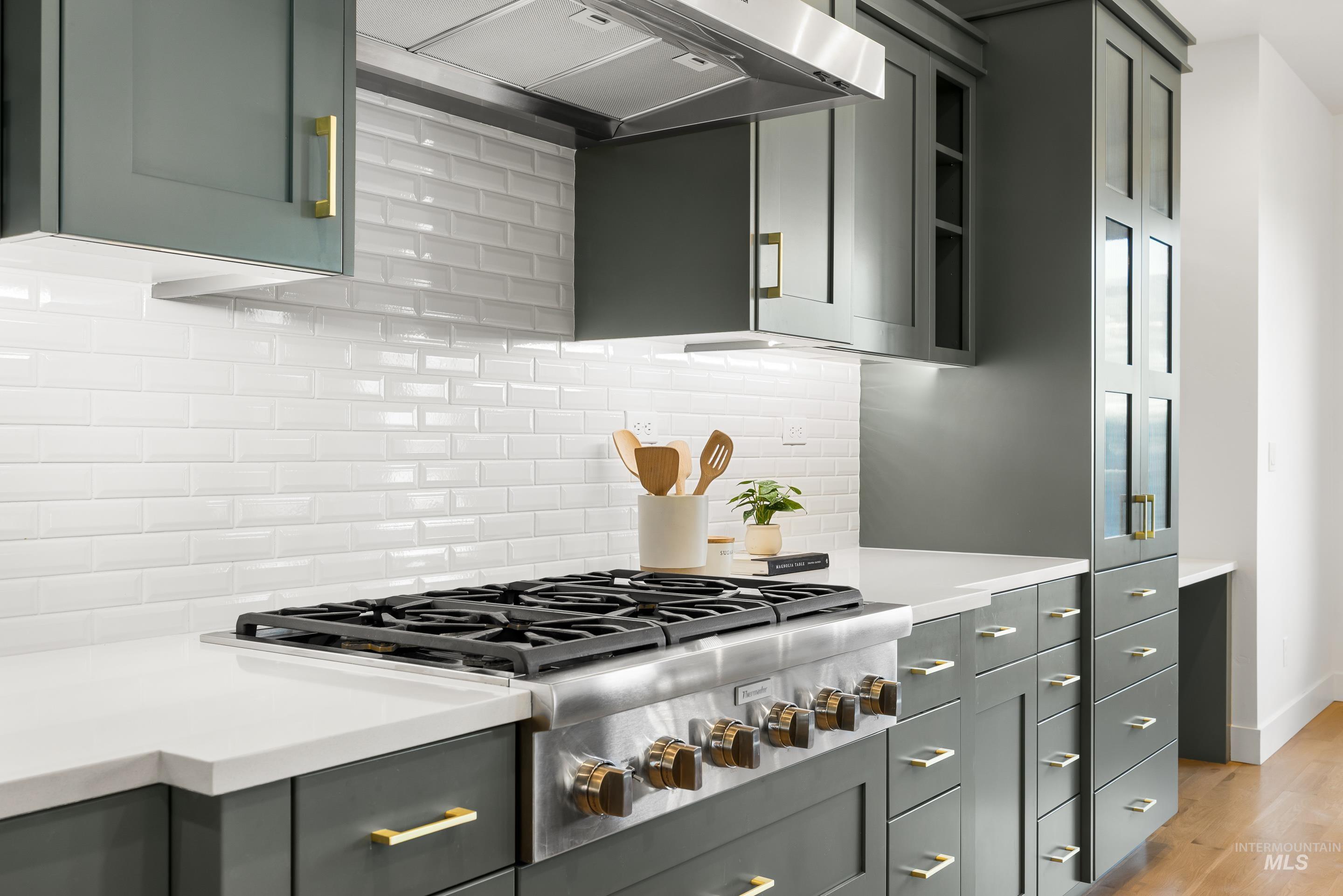 Kitchen with stainless steel gas stovetop, premium range hood, light wood finished floors, tasteful backsplash, and gray cabinetry