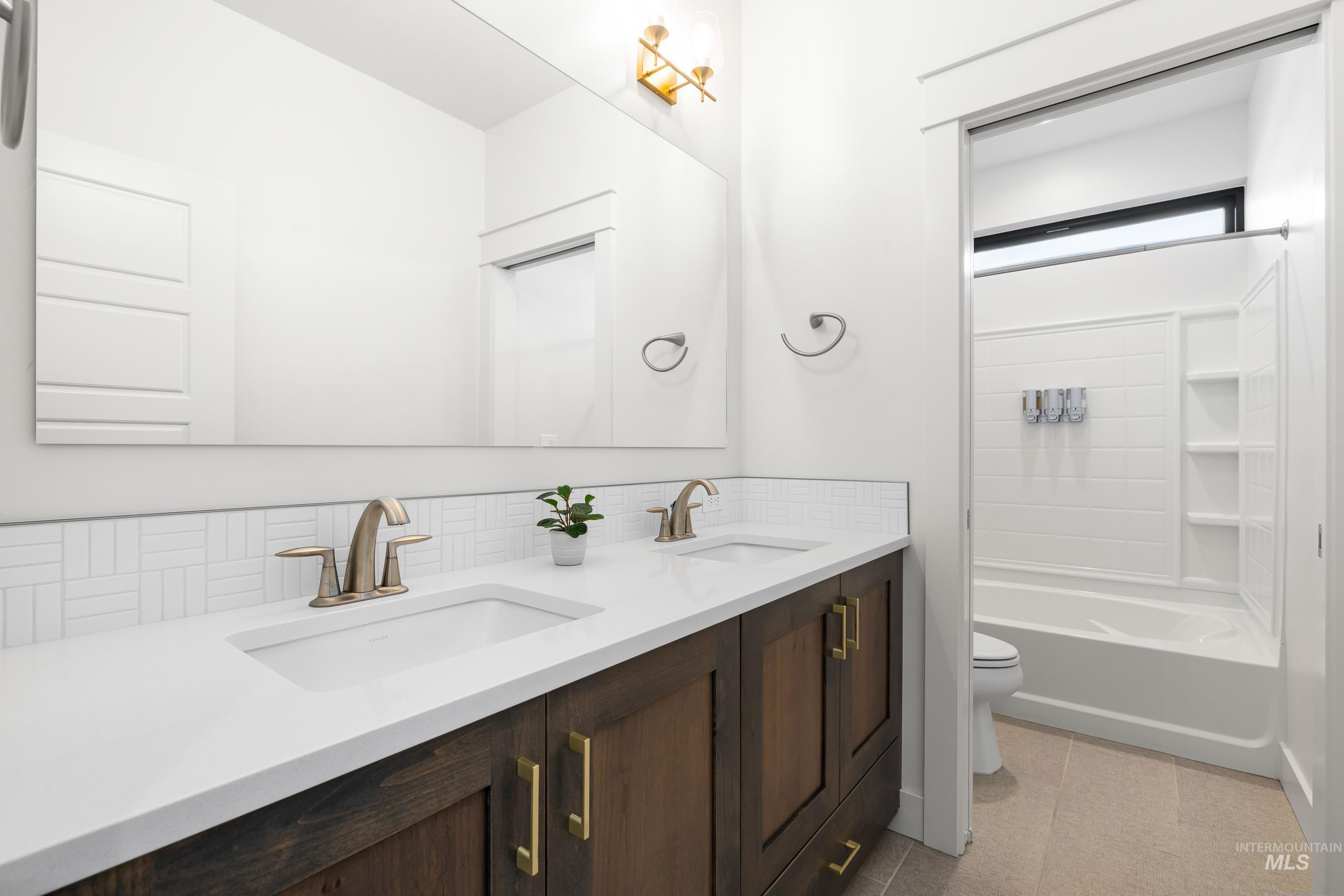Full bathroom featuring double vanity, backsplash, and shower / bath combination