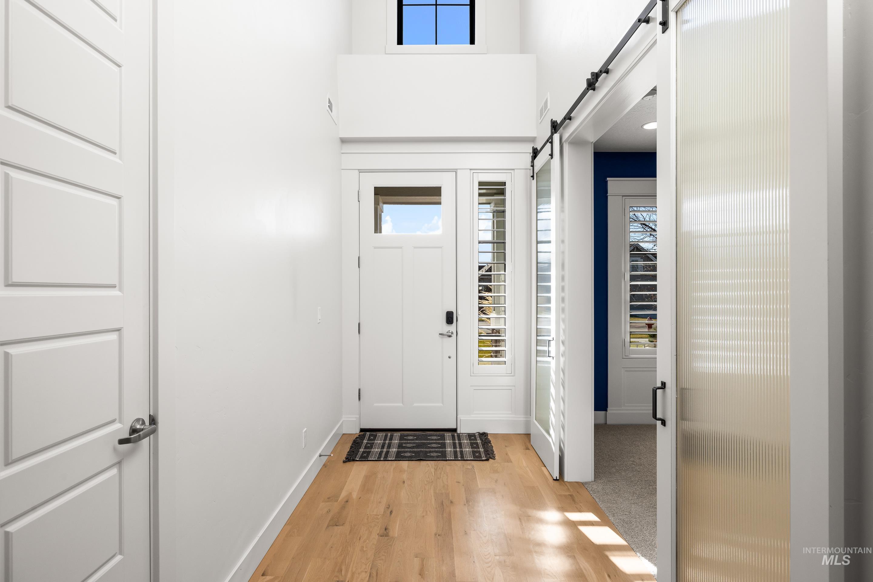 Entryway with a barn door, plenty of natural light, light wood finished floors, and a towering ceiling