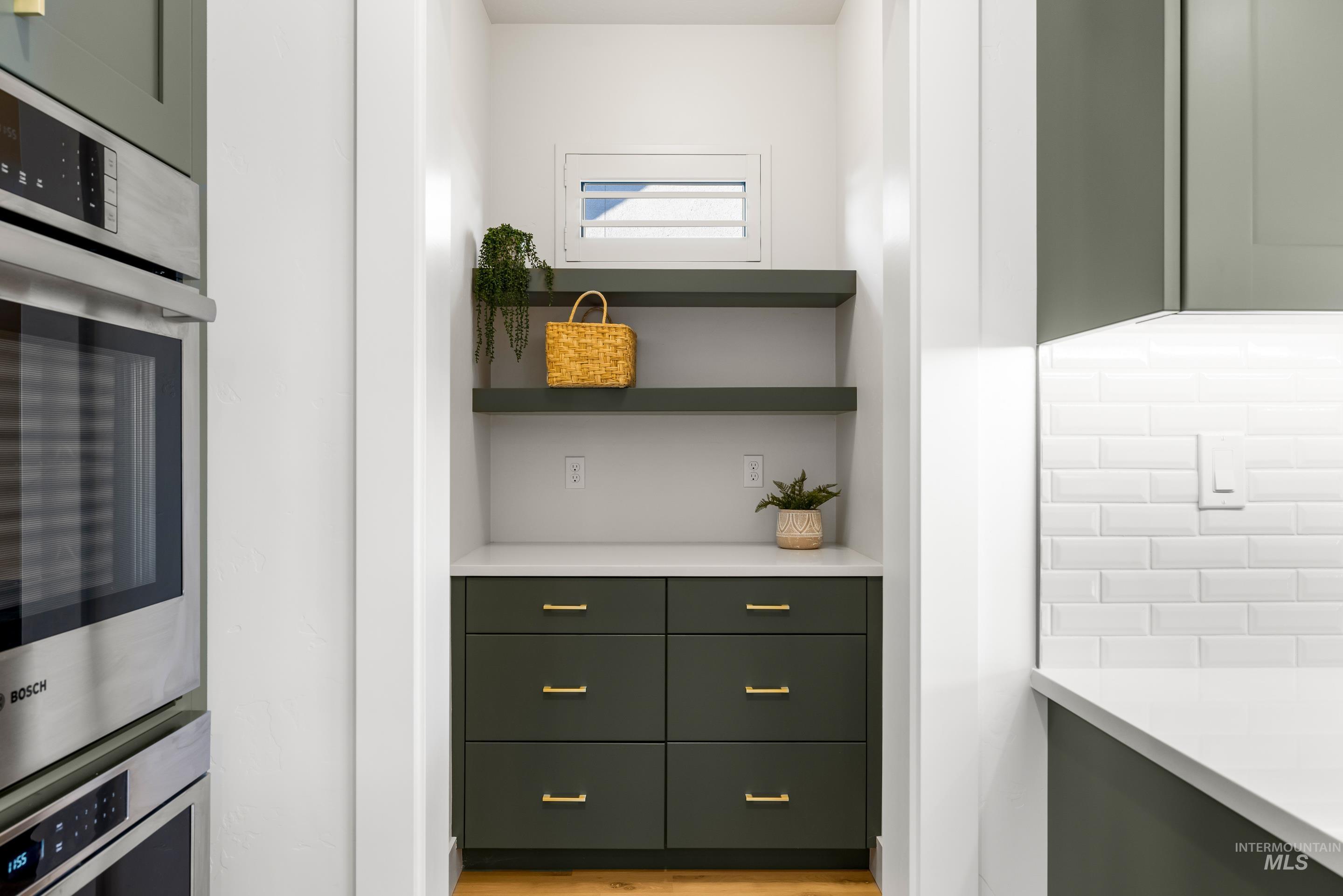 Bar with open shelves, stainless steel double oven, green cabinetry, and light stone counters
