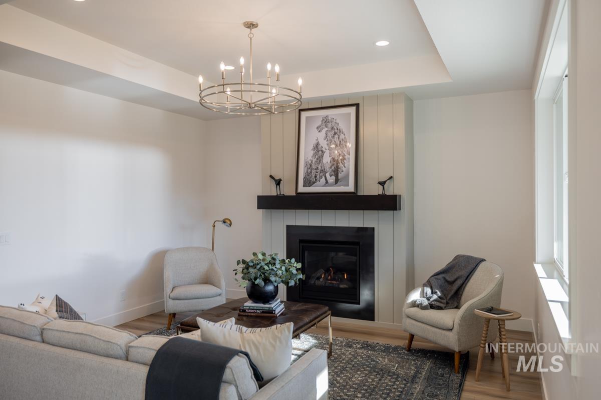 Living room with a fireplace, wood finished floors, a chandelier, a raised ceiling, and recessed lighting