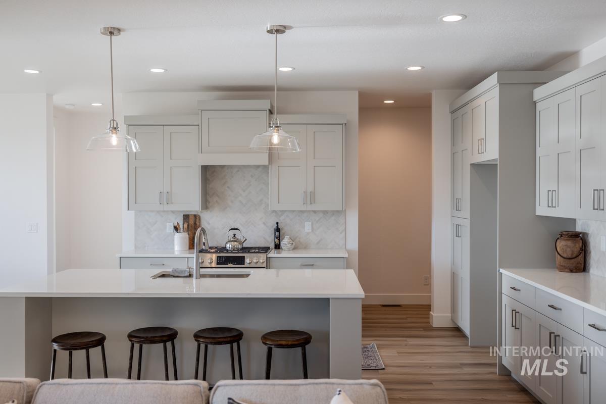 Kitchen featuring a breakfast bar, light stone counters, tasteful backsplash, light wood-style floors, and decorative light fixtures