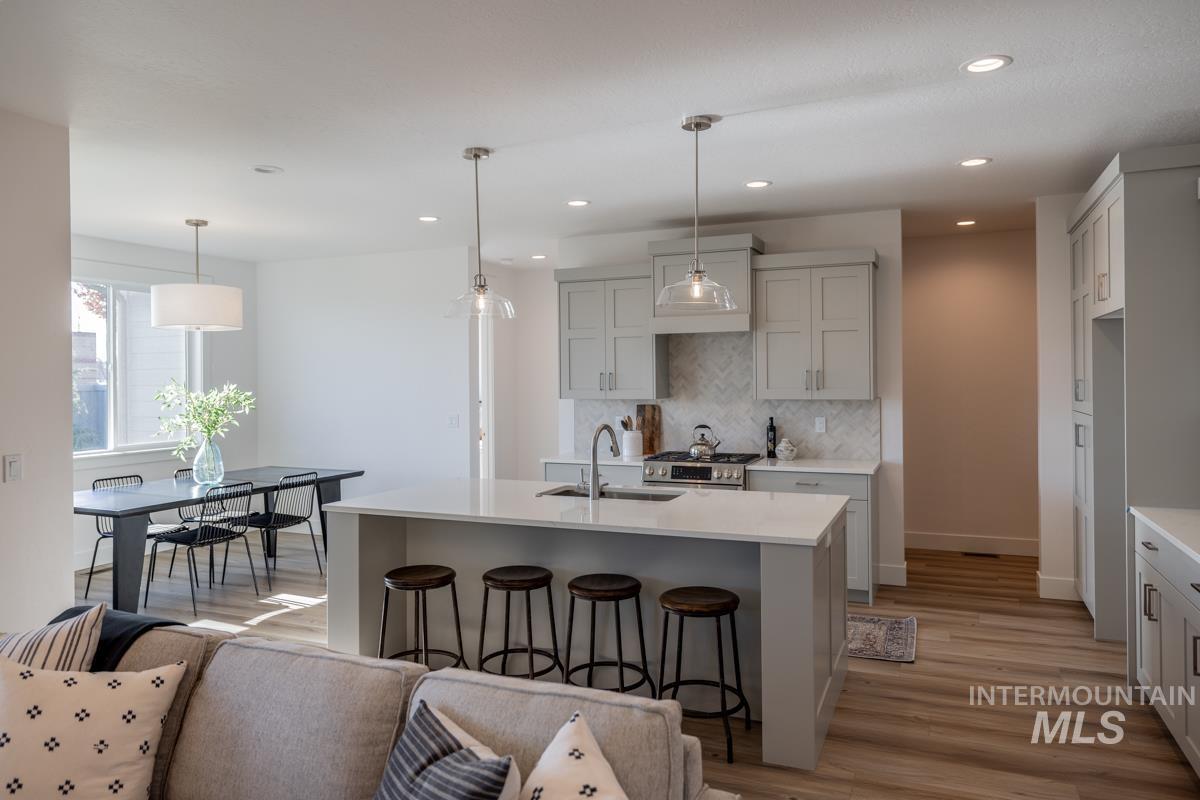 Kitchen featuring a breakfast bar, decorative light fixtures, decorative backsplash, a center island with sink, and light wood-type flooring