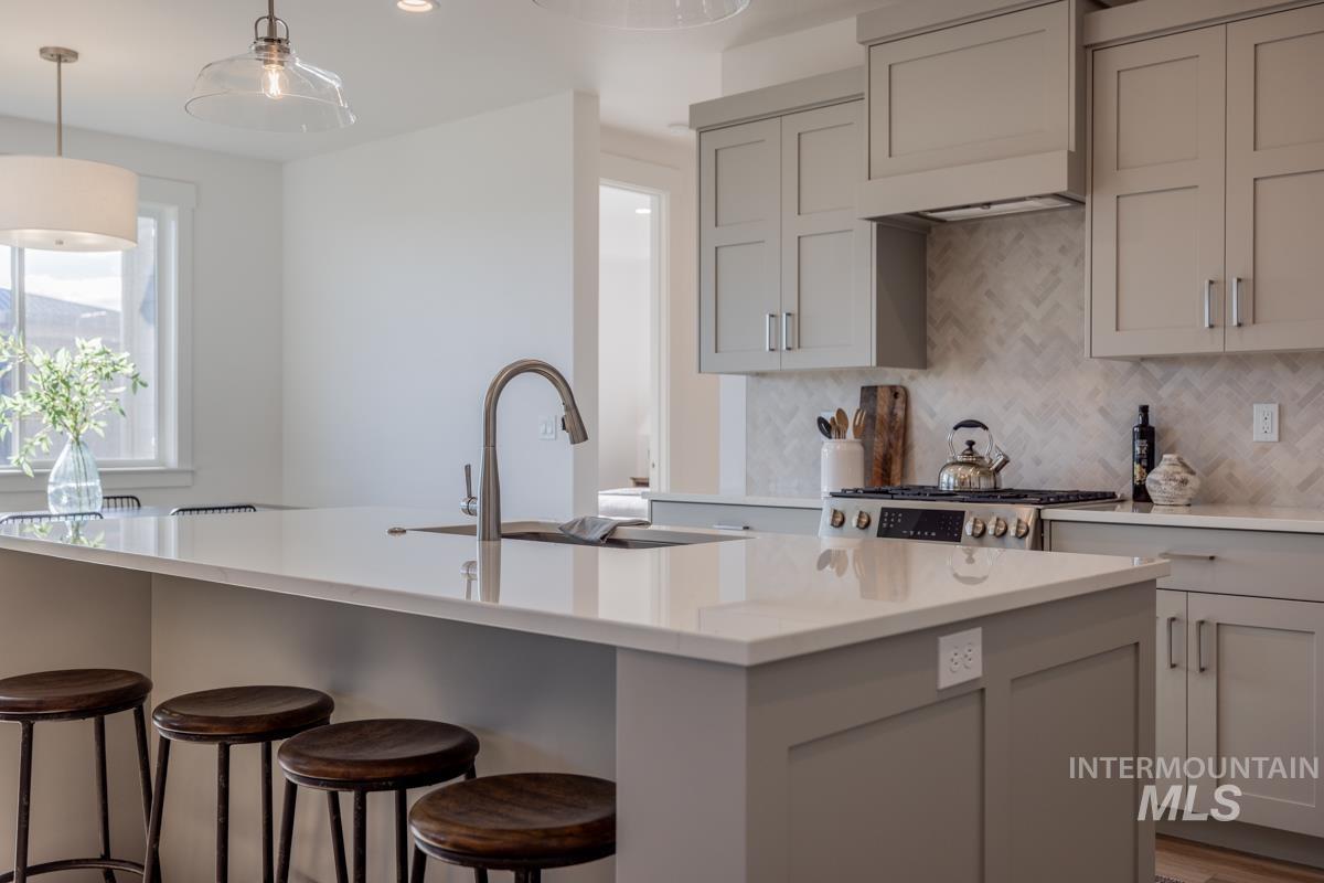 Kitchen with gray cabinets, tasteful backsplash, hanging light fixtures, and light stone countertops