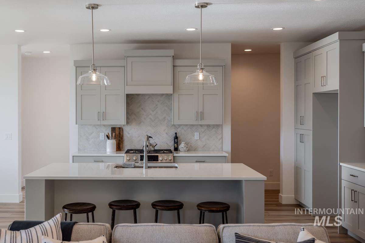 Kitchen with decorative light fixtures, a kitchen breakfast bar, backsplash, light stone countertops, and recessed lighting