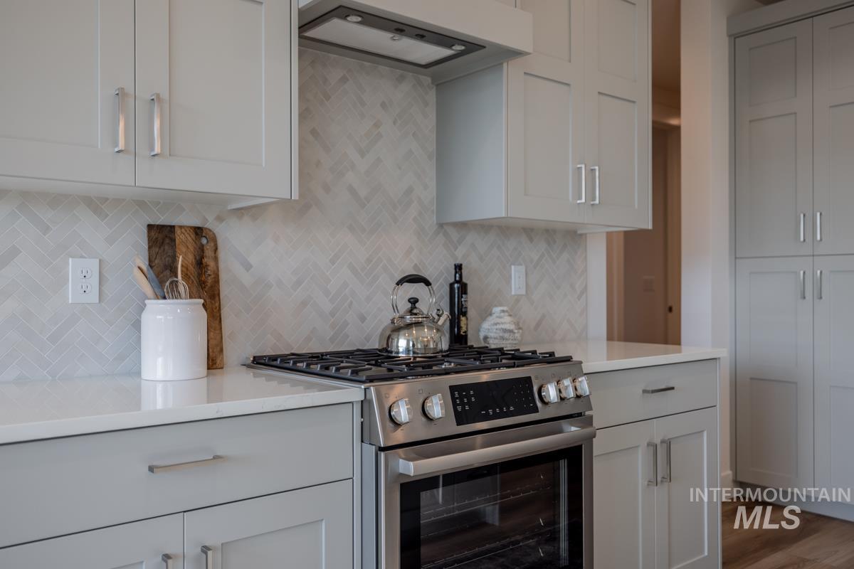 Kitchen with gas range, premium range hood, light stone counters, white cabinetry, and backsplash
