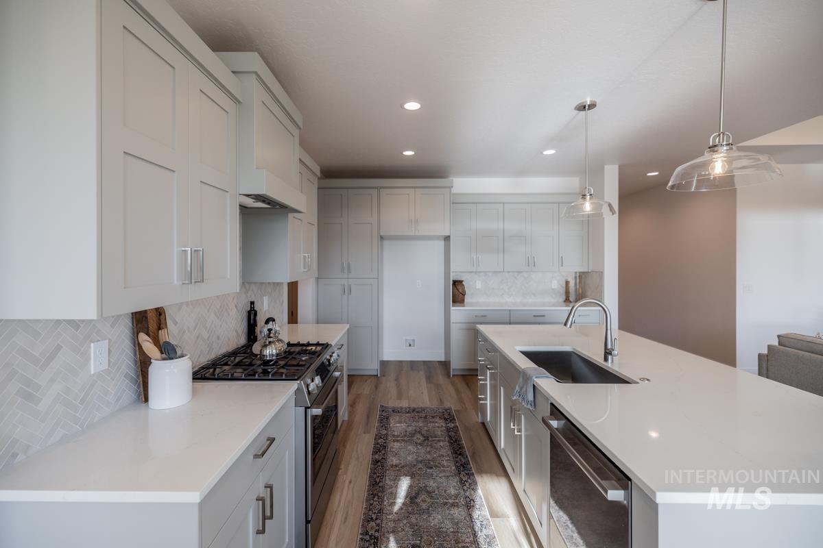 Kitchen with appliances with stainless steel finishes, decorative light fixtures, backsplash, a large island with sink, and light wood-style flooring
