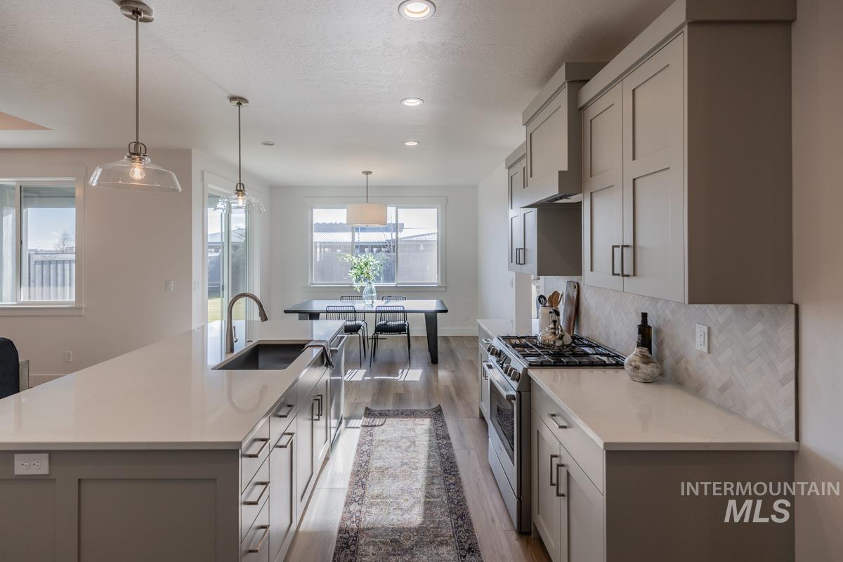 Kitchen featuring stainless steel gas stove, hanging light fixtures, gray cabinets, light wood-style floors, and an island with sink