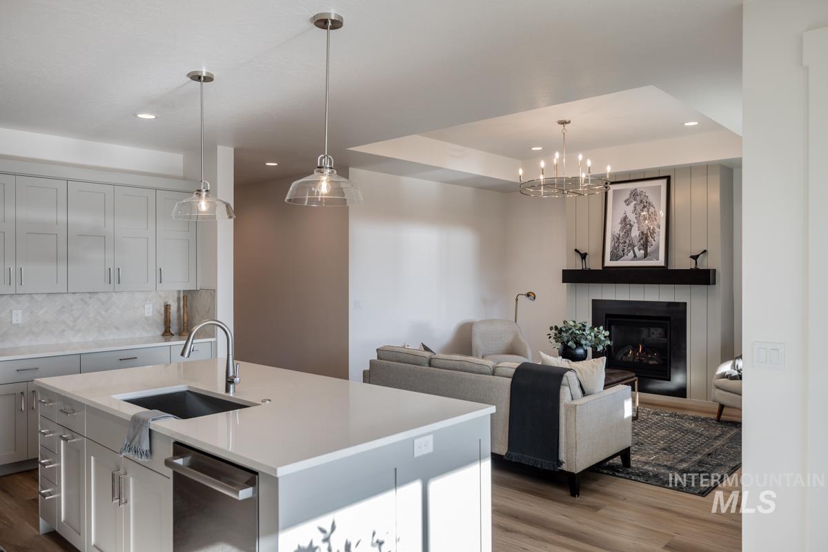 Kitchen featuring a fireplace, backsplash, a center island with sink, dishwasher, and gray cabinetry