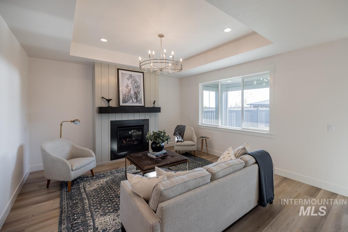 Living area featuring recessed lighting, a tray ceiling, light wood-type flooring, a fireplace, and a chandelier