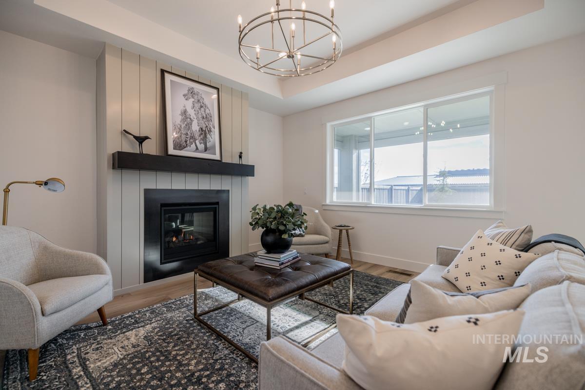Living room with a tray ceiling, a large fireplace, wood finished floors, and a chandelier