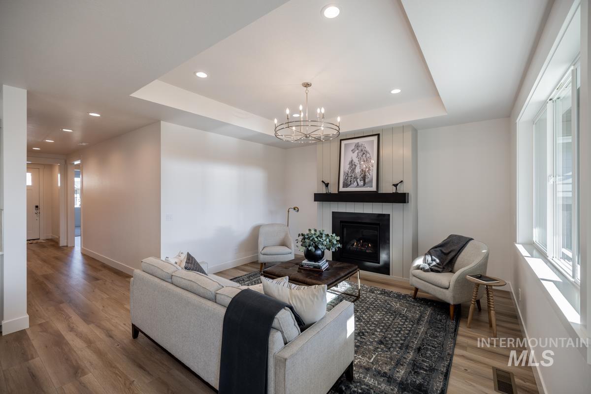 Living area with recessed lighting, a chandelier, a large fireplace, a raised ceiling, and wood finished floors