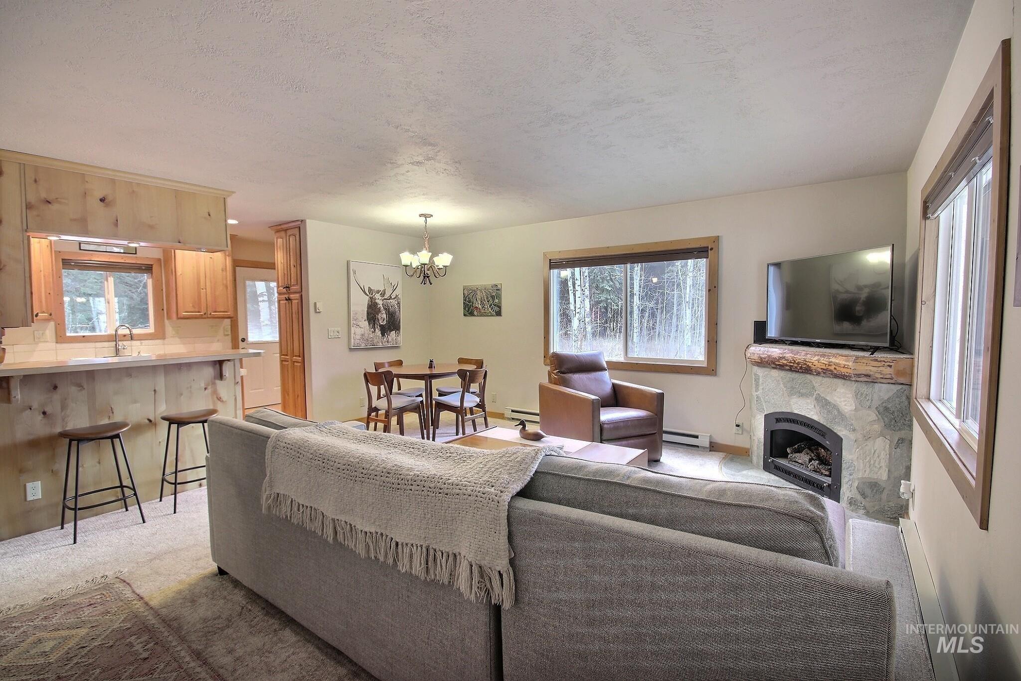 Living area featuring a fireplace, light colored carpet, baseboard heating, a chandelier, and a textured ceiling