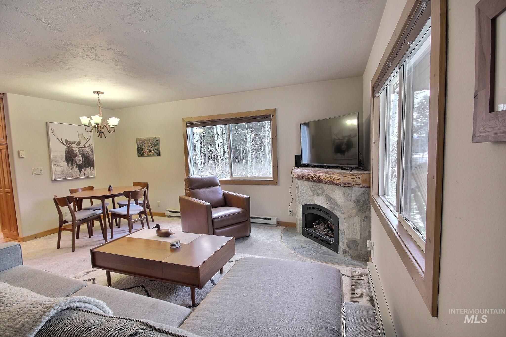 Living room with plenty of natural light, a tiled fireplace, a baseboard radiator, a chandelier, and a textured ceiling