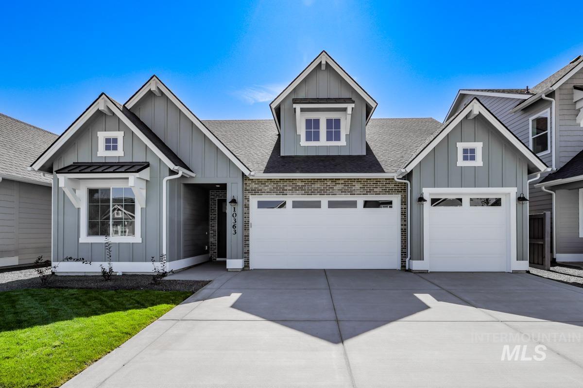 View of front of property featuring board and batten siding, driveway, a shingled roof, a front yard, and brick siding