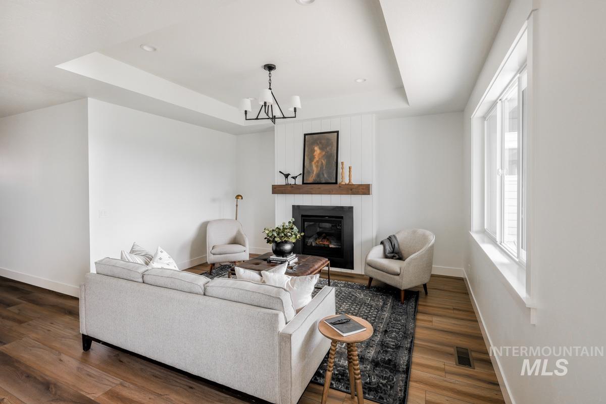 Living area featuring a fireplace, a raised ceiling, recessed lighting, wood finished floors, and a chandelier