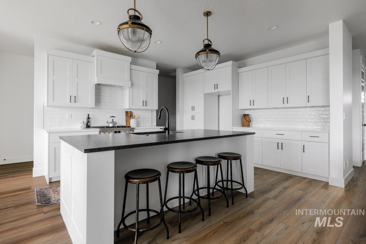 Kitchen with dark countertops, a kitchen breakfast bar, white cabinets, an island with sink, and decorative backsplash