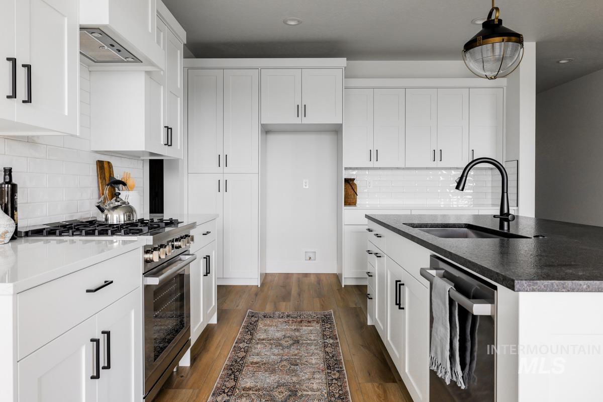 Kitchen featuring stainless steel appliances, white cabinetry, wall chimney exhaust hood, a kitchen island with sink, and backsplash