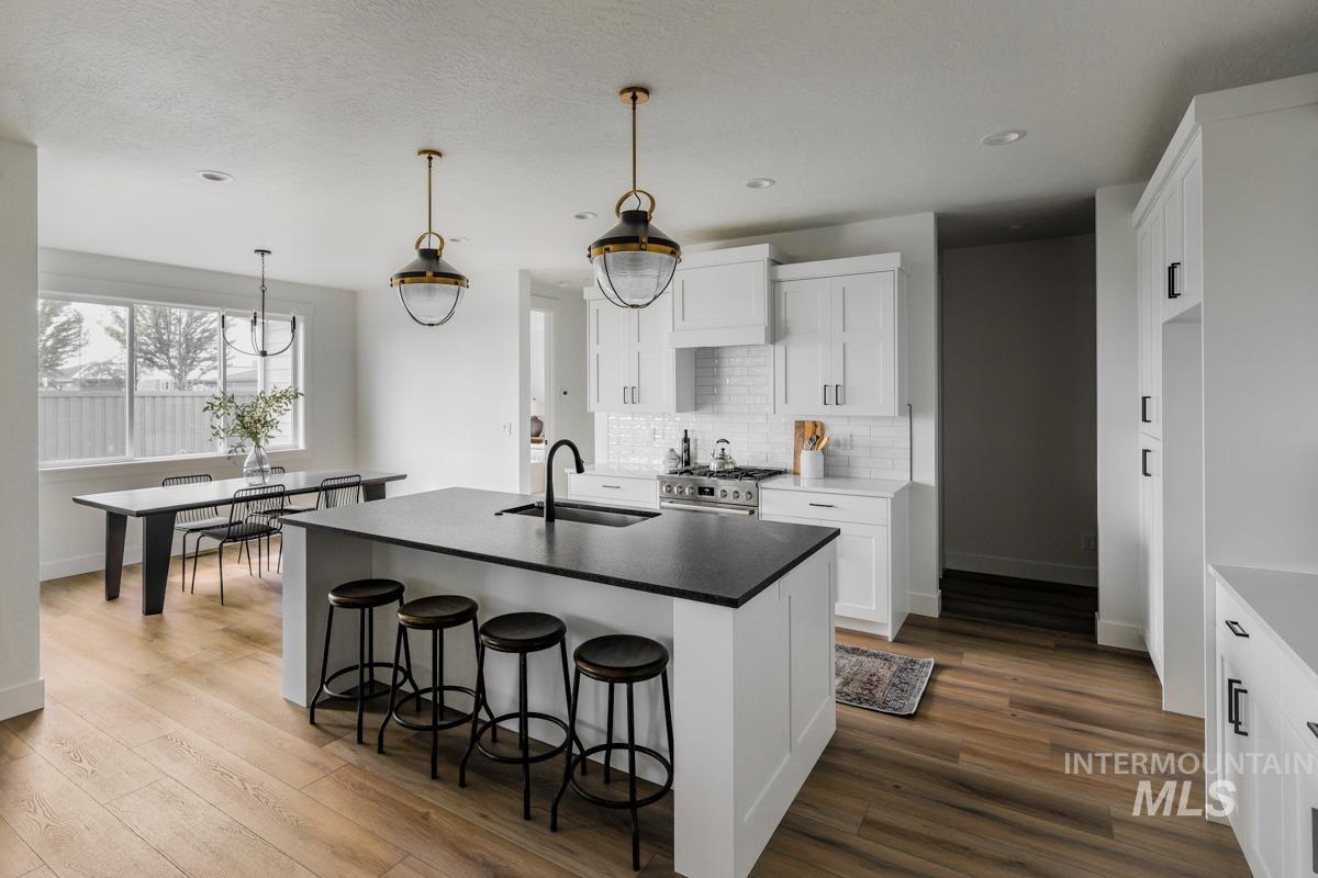 Kitchen featuring a kitchen island with sink, backsplash, a kitchen breakfast bar, white cabinetry, and stainless steel stove