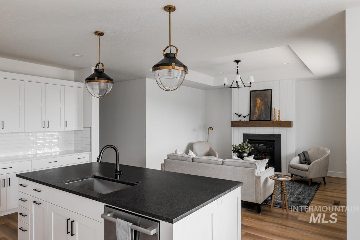 Kitchen with white cabinetry, a large fireplace, stainless steel dishwasher, hanging light fixtures, and dark wood-style flooring