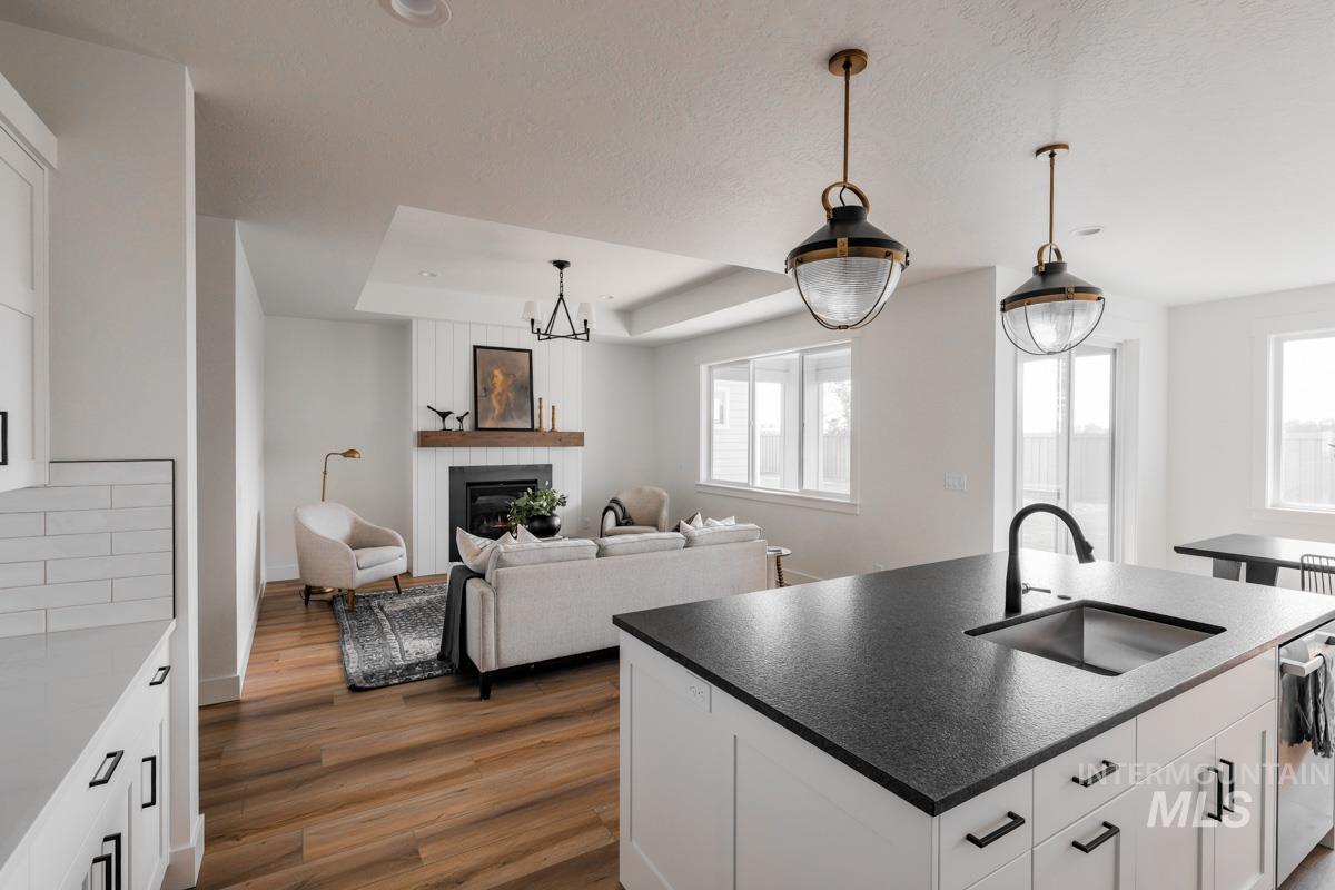 Kitchen with white cabinets, a center island with sink, a large fireplace, dark wood finished floors, and hanging light fixtures