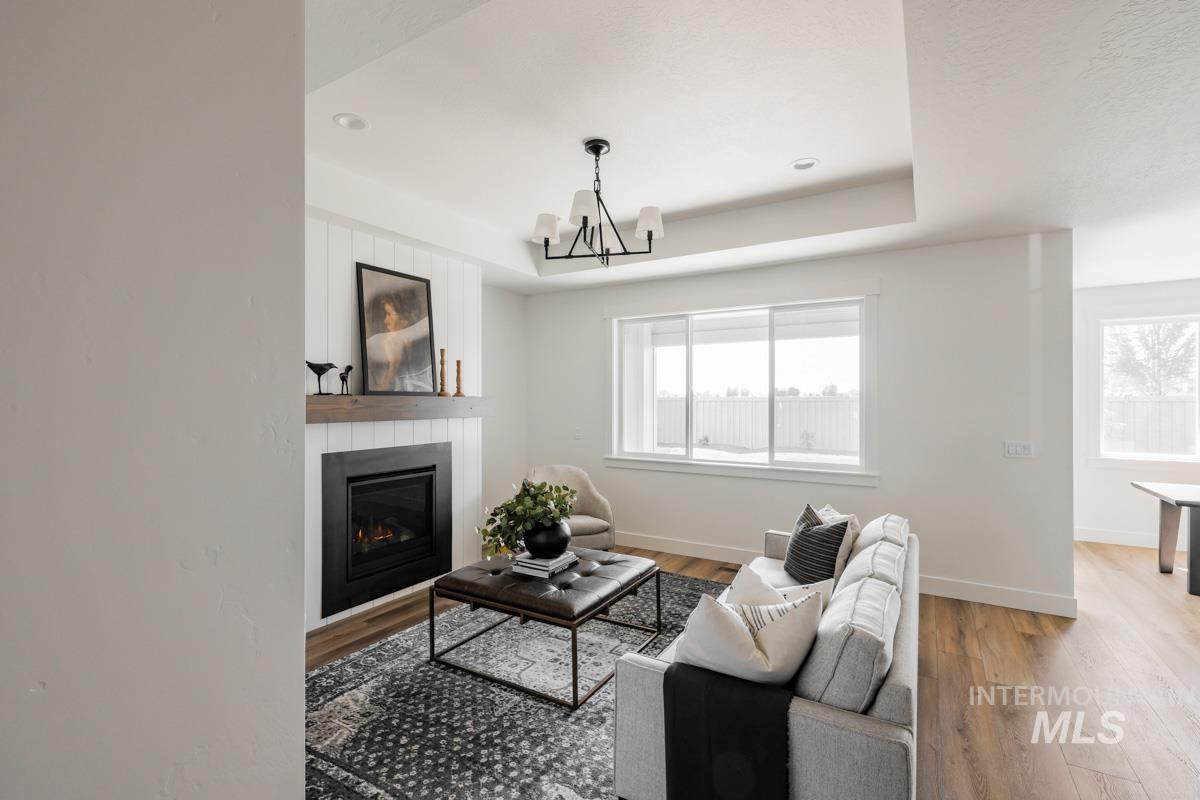 Living area with a tray ceiling, wood finished floors, a glass covered fireplace, and a chandelier