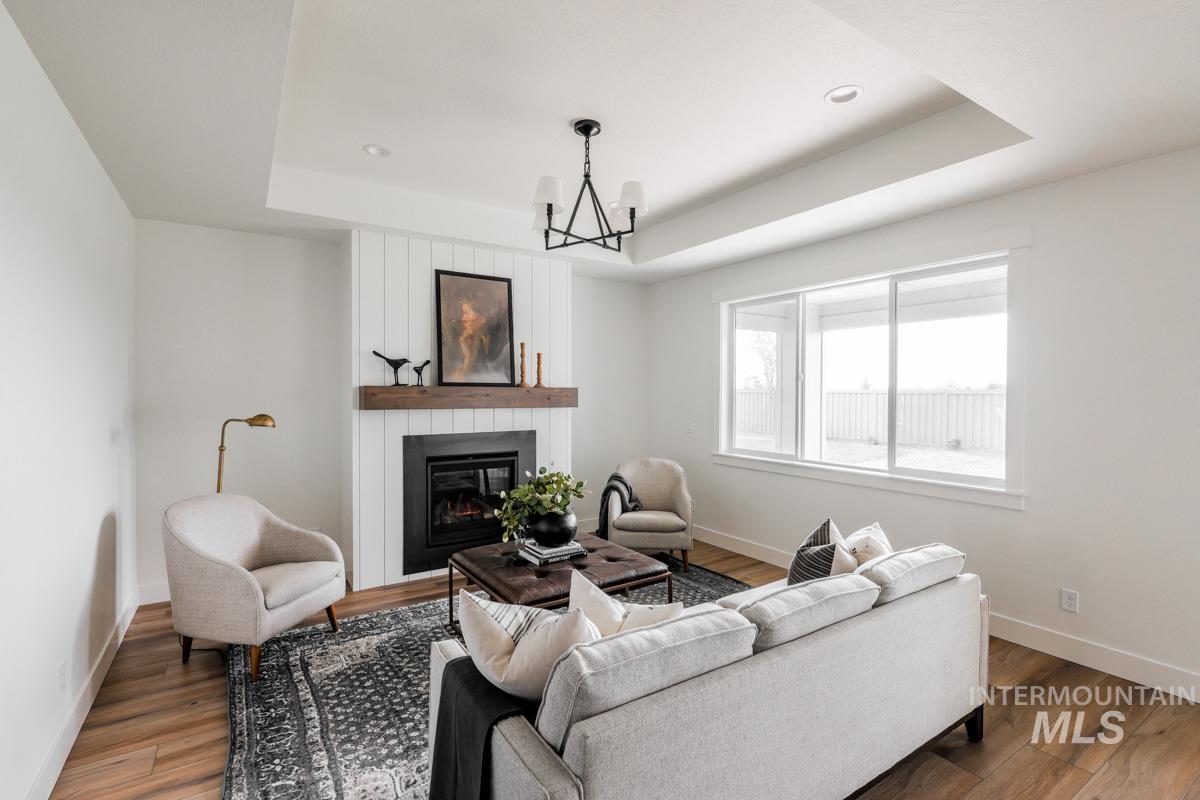 Living area with a raised ceiling, a fireplace, wood finished floors, a chandelier, and recessed lighting