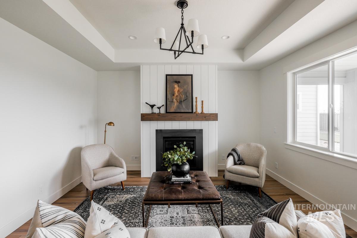 Living area featuring a large fireplace, a chandelier, wood finished floors, a tray ceiling, and recessed lighting