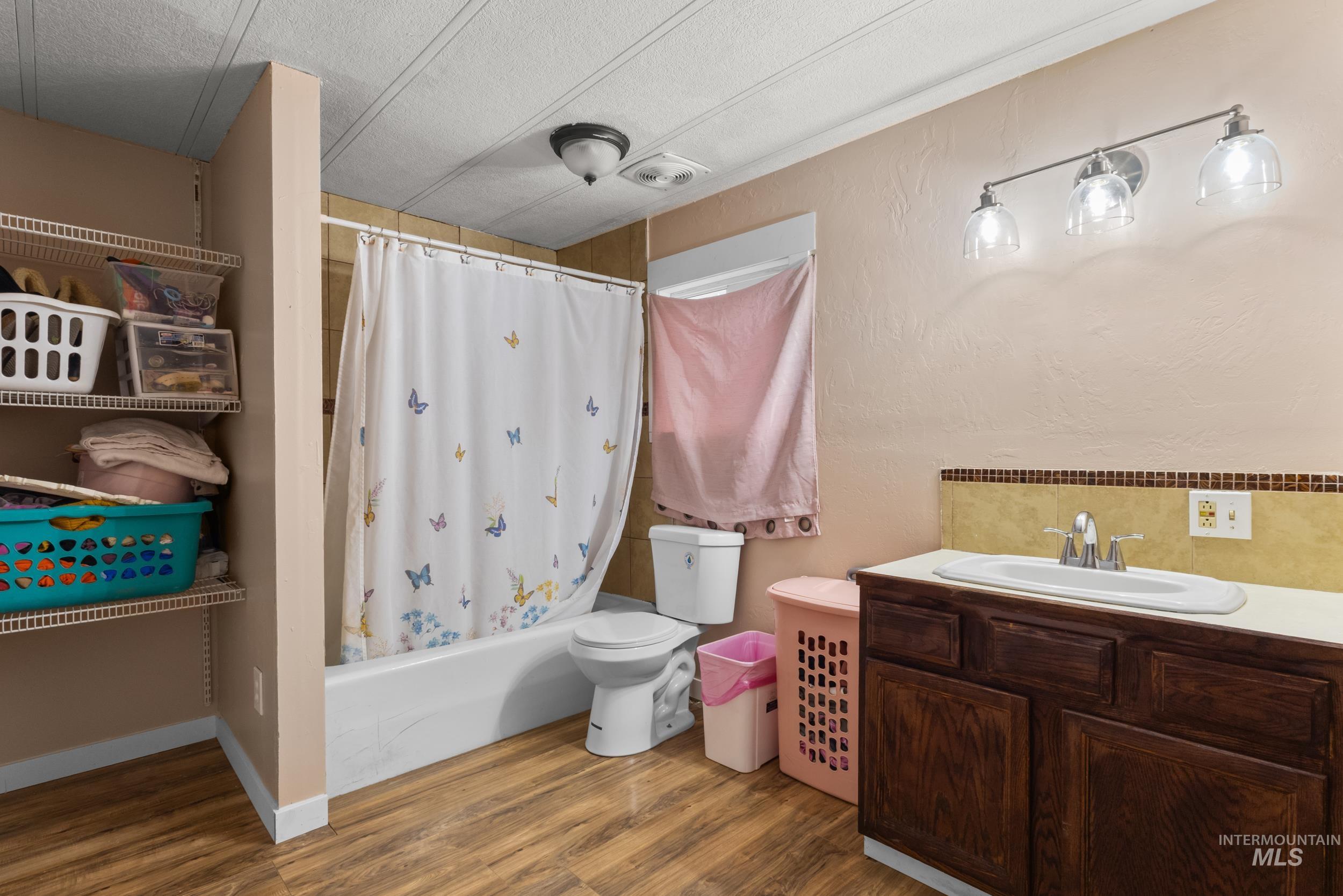 Bathroom with vanity, wood finished floors, shower / bath combo, and a textured ceiling