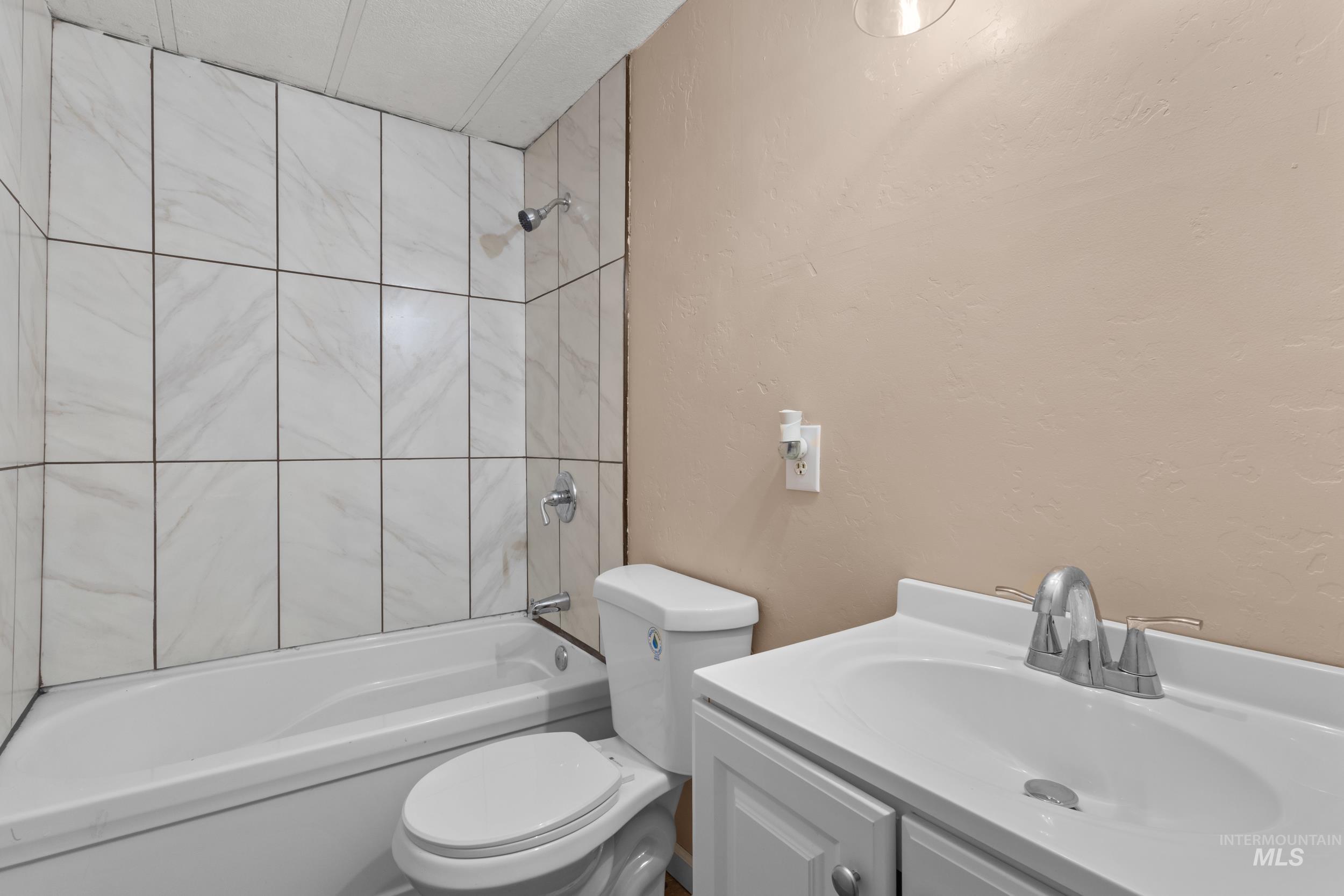 Full bathroom with a textured wall, shower / tub combination, and vanity