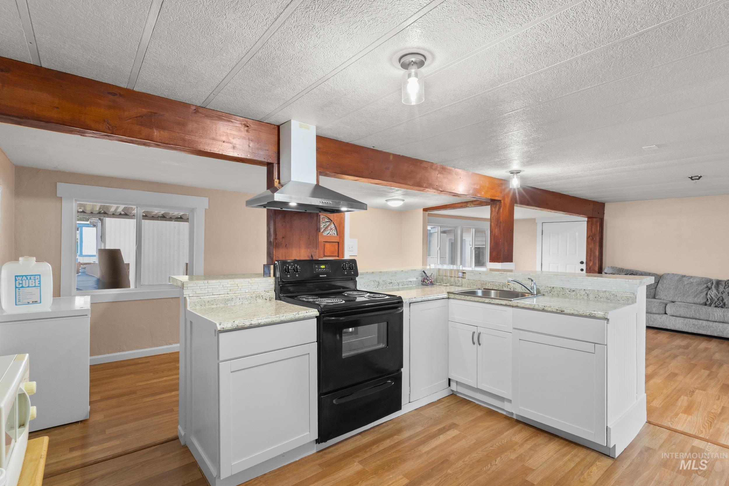 Kitchen with open floor plan, electric range, exhaust hood, white cabinets, and light wood-style flooring